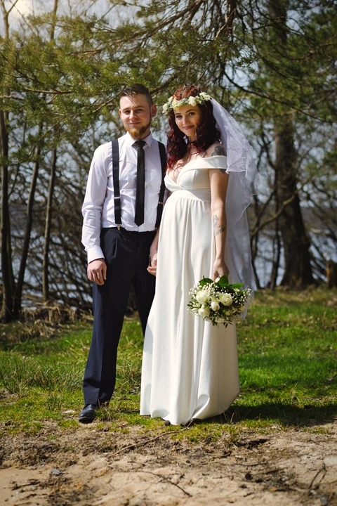 Nevěsta se ženichem se drží za ruku a koukají na fotografa, portrét