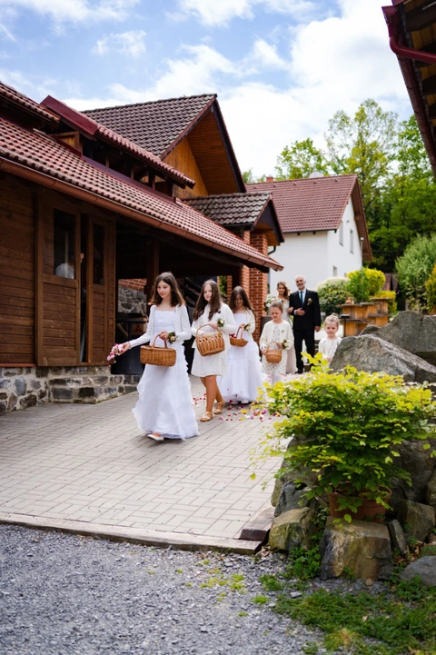 Družičky jdou před nevěstou a sypou na zem okvětní lístky, svatba na farmě v Herouticích.
