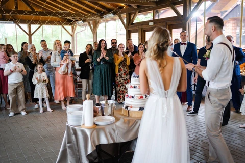 Svatebčané tleskají novomanželům zatímco krájí dort, farma Heroutice.