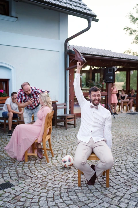 Ženich se směje zatímco zvedá botu nad hlavu, svatební hra