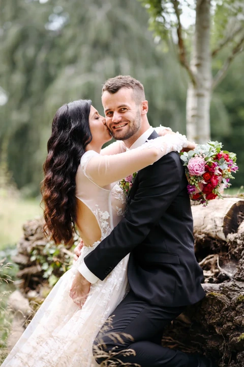 Nevěsta líbá ženicha a ten se kouká na fotografa, portrét