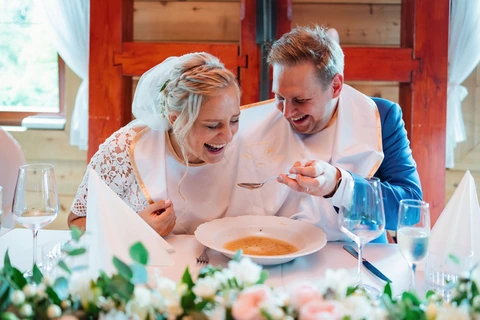 Ženich s nevěstou se smějí zatímco jedí polévku, svatba Golf resort Kunětická hora