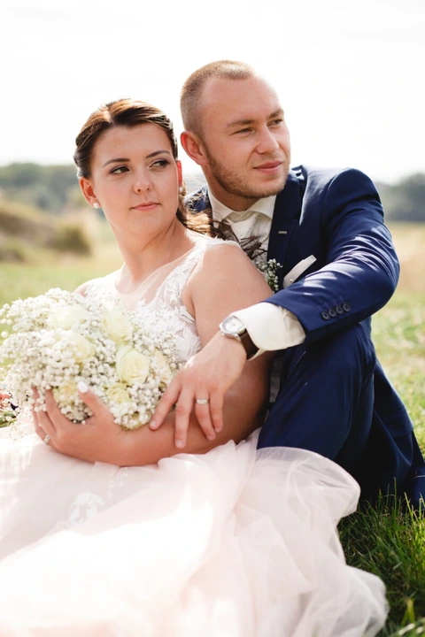 Nevěsta se ženichem sedí v trávě a koukají do dáli, detail