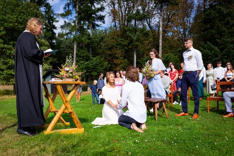Nevěsta se ženichem během obřadu klečí v trávě a drží se za ruce