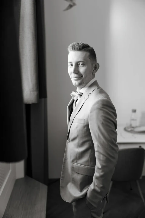Ženich stojí u okna a kouká na fotografa