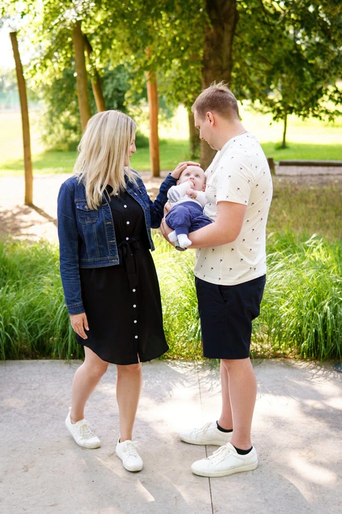Tatínek drží syna v náručí a maminka jej hladí po hlavě. Rodinné focení v parku.