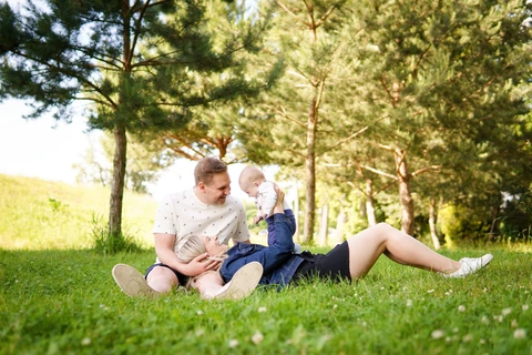 Maminka leží opřená o tátu a zvedá synka, rodinné focení v parku.