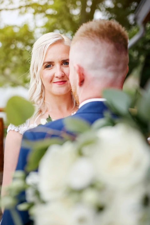 Detail nevěsty, jak kouká na fotografa přes ženichovo rameno