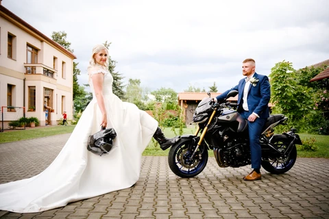 Nevěsta se opírá nohou o přední kolo motorky zatímco ženich sedí na motorce a kouká na nevěstu, svatba Lhota pod Libčany