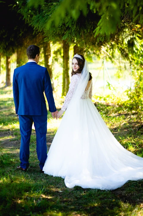 Nevěsta se ženichem stojí na lesní cestě zády k fotografovi a nevěsta se dívá na fotografa