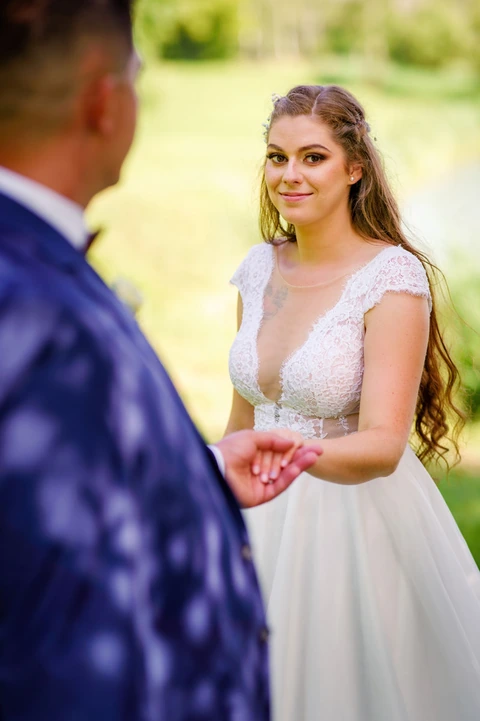 Nevěsta kouká na fotografa zatímco jí ženich drží za ruku