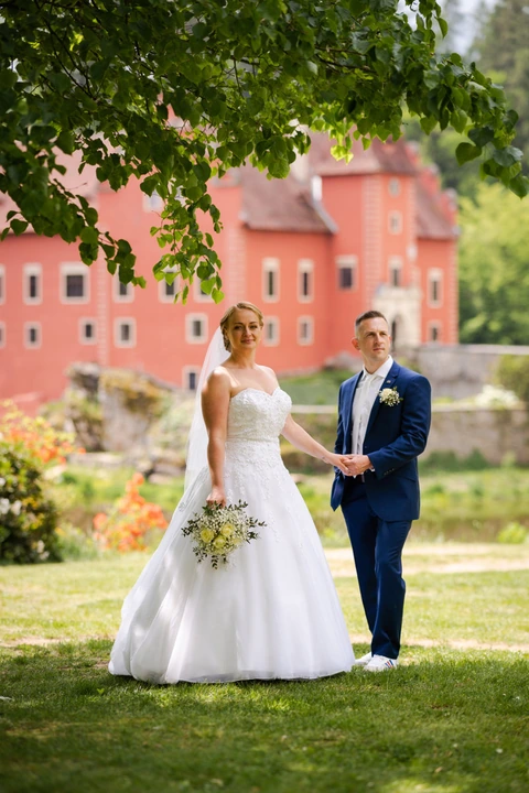 Nevěsta kouká na fotografa zatímco jí drží za ruku ženich, zámek Červená Lhota